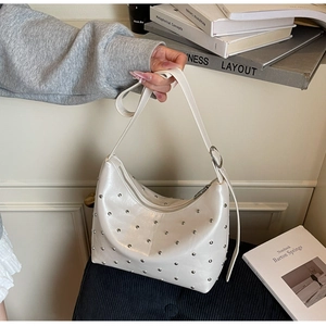 Detail of off-white faux leather shoulder bag featuring silver rivets and adjustable strap