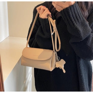 Detail of beige lychee leather crossbody bag with elephant charm and flap design