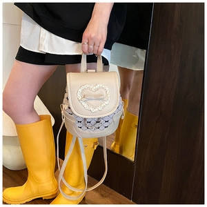 Detail of a mini beige backpack featuring lace heart trim, leather bow, and chain accents