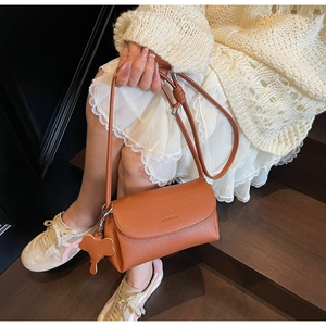 Detail of brown litchi leather underarm bag featuring logo embossing and elephant charm