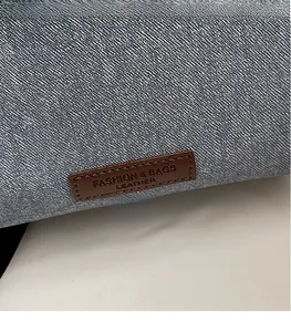 Detail of a brown leather embossed logo patch on a textured blue denim fabric bag