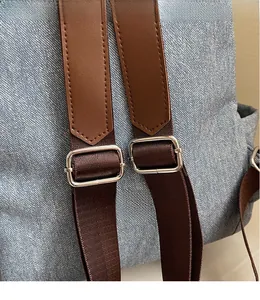 Detail of adjustable denim backpack strap with brown leather and silver metal buckle