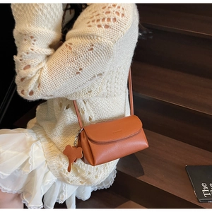 Detail of a brown leather underarm bag featuring a cute elephant charm on white outfit