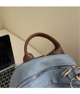 Detail of light blue denim backpack with brown leather handle and silver metal zipper