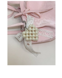 Detail eines Perlenherz-Anhängers mit weißer Spitzen-Schleife an einer rosa Tasche