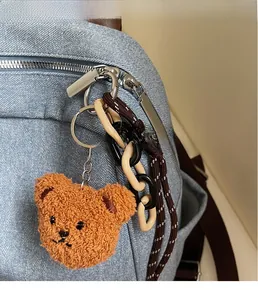 Close-up of a teddy bear plush charm with metal rings on a blue denim backpack