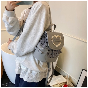 Detail of grey mini backpack with lace heart, bow accent, and metal chain decoration