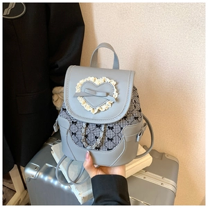 Detail of light blue mini backpack with heart lace, bow accents and metal chain on a suitcase