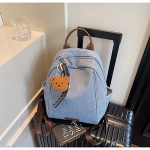 Detail of light blue denim backpack with brown leather straps and cute plush bear charm
