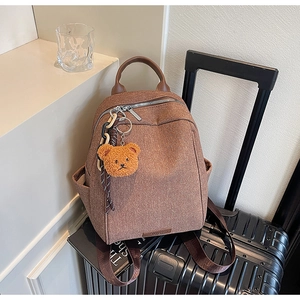 Close-up of brown canvas backpack with leather handle and a cute bear charm accessory