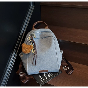 Detail of light blue textured denim backpack with leather handle and cute bear charm