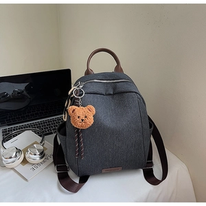 Detail of dark grey canvas backpack with brown leather handle and cute bear charm pendant