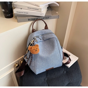 Close-up of light blue denim backpack featuring leather straps and a cute brown bear charm