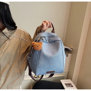 Detail of light blue denim texture backpack with brown handles and a plush bear charm