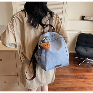 Close-up of light blue denim backpack with brown leather handle and cute bear charm