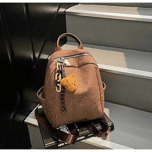 Detailed texture of dark brown canvas backpack with leather handle and teddy bear charm
