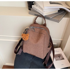 Brown canvas backpack with leather handles and a plush bear charm in a lifestyle setting