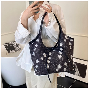 Close-up of black tweed tote bag featuring white 3D floral accents and leather bow detail