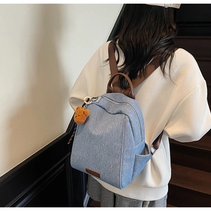 Detail of denim backpack with brown leather straps and a yellow plush bear charm