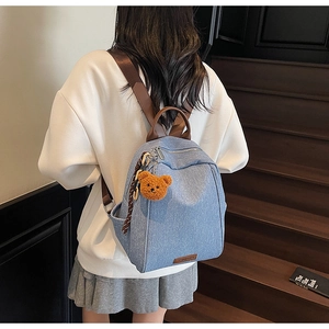 Denim backpack with brown leather straps and cute bear charm shown in a cozy indoor setting