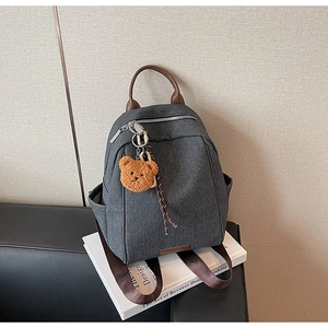Detail of grey canvas backpack with leather handle and cute brown bear plush charm