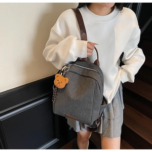 Detail of dark gray denim backpack with brown leather straps and cute plush bear charm