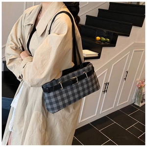 Detail of checkered baguette bag with silver buckles on a neutral staircase backdrop