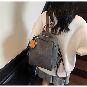 Detail of grey fabric backpack with brown leather straps and cute plush bear charm accessory