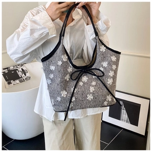 Detail of grey tweed tote bag featuring white floral accents and a black bow ribbon charm
