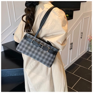 Detailed view of black and gray checkered baguette bag with leather strap on shoulder