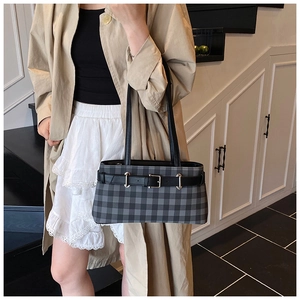 Detail of plaid baguette bag featuring black leather strap and silver metal buckle accent