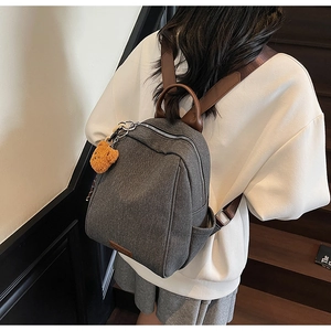 Detail of grey canvas mini backpack with brown leather straps and yellow bear pendant