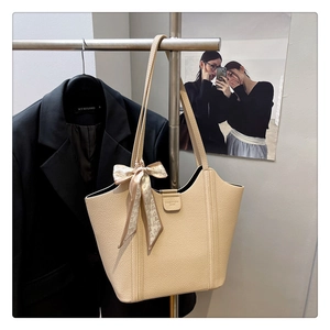 Close-up of beige leather tote bag featuring a decorative heart scarf and fashion buckle