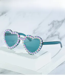 Detail of heart-shaped teal sunglasses with iridescent AB rhinestones on a white stand