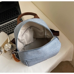 Detail of light blue denim backpack interior with cream lining and brown leather handle