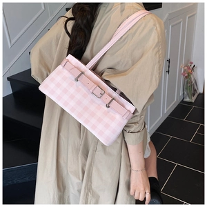 Detail of pink plaid baguette bag with silver buckles worn over a khaki trench coat