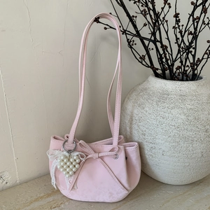 Rosa plissierte Handtasche mit großer Schleife und Perlenherz auf Marmorfläche