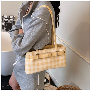 Detail of yellow checkered baguette bag featuring a decorative belt buckle and double straps