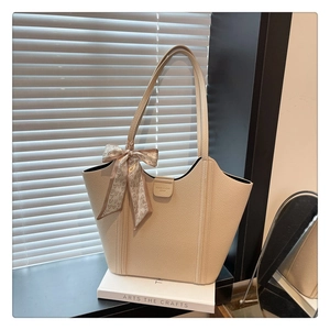 Detail of beige lychee textured tote bag with heart print scarf on white books