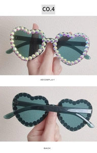 Detailed view of heart-shaped sunglasses with rainbow rhinestones and green lenses