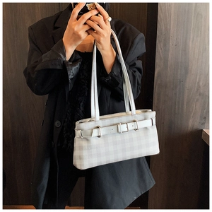 Detail of checkered baguette bag with buckle accents worn by a model in a blazer