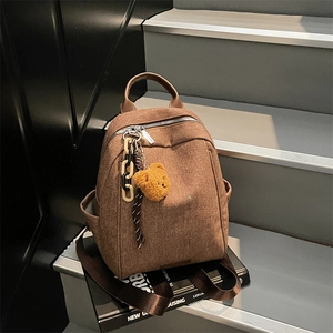 Brown textured backpack with teddy bear charm on black magazine, minimalist city style