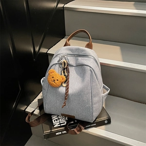 Minimalist light blue denim backpack with brown leather straps and a cute plush bear charm