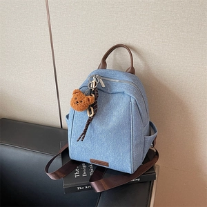 Minimalist denim backpack with leather straps and bear charm shown on a design book