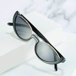 Lunettes de soleil œil de chat rétro avec monture noire et détails dorés sur marbre blanc