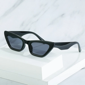 Retro black cat-eye sunglasses with dark grey lenses on a white geometric display stand