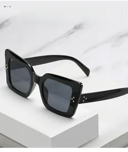 Close-up of black glossy cat-eye sunglasses featuring golden triple metal rivets detail