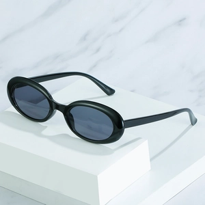 Classic black oval sunglasses with dark gray lenses on a minimalist white marble base