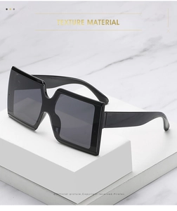 Detailed close-up of chunky square black frame sunglasses on a marble stand