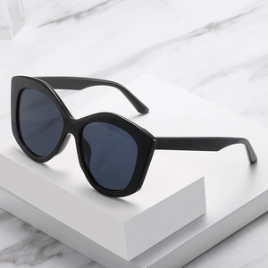 Lunettes de soleil cat-eye surdimensionnées noires avec verres gris sur marbre blanc